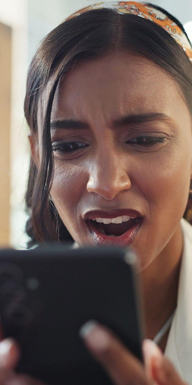 Woman looking at her phone with a shocked look on her face.
