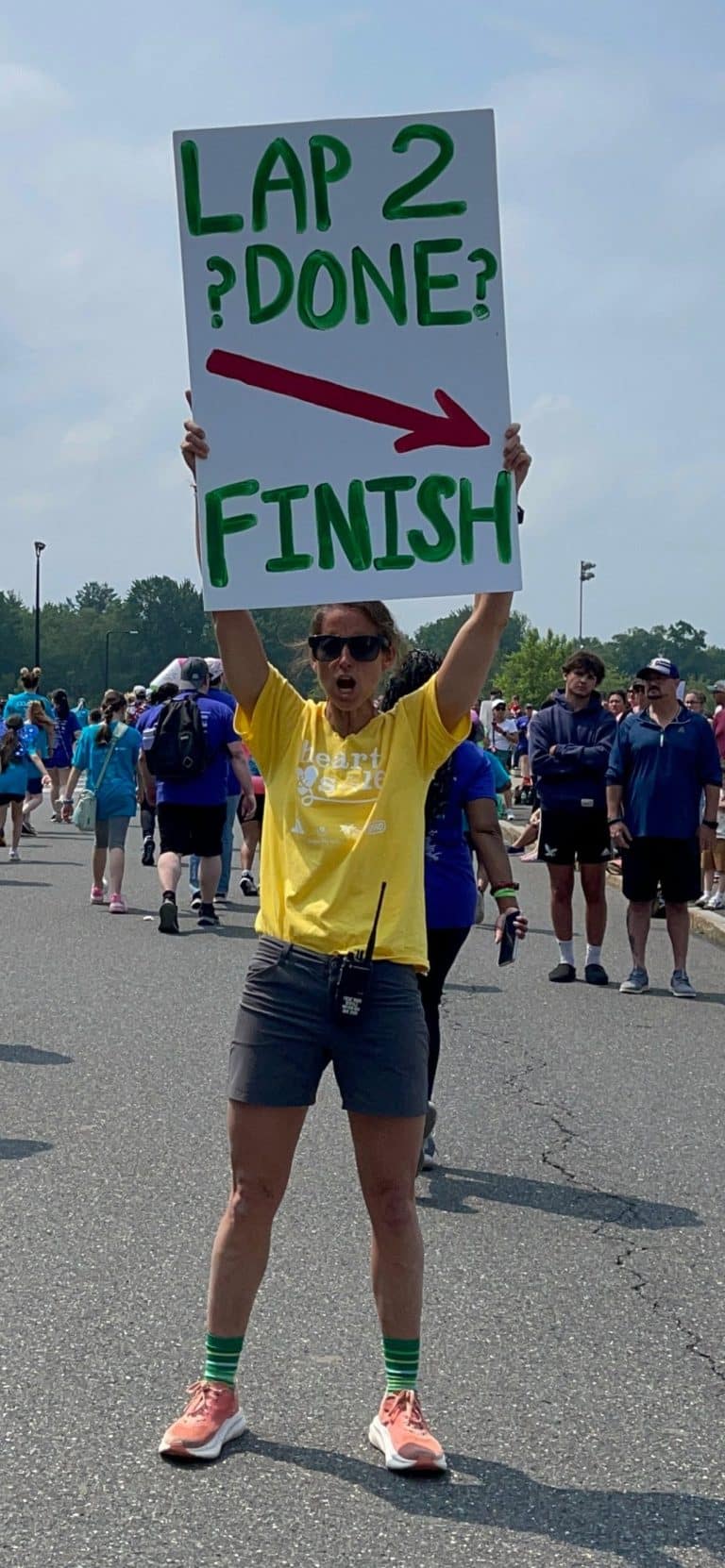 An event marshall at the Girls on The Run event holds up a directional sign. UMass Amherst, June 8, 2024. FungaiFoto